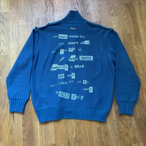 Blå tröja från Richmond   - Säljer en blå tröja med unika textdetaljer på baksidan. Tröjan har en dragkedja framtill och ribbade muddar vid ärmslut och nederkant. Perfekt för en fräsch stil med en twist.