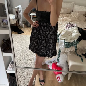 Svart paljettklänning med spetsdetaljer - Snygg svart klänning med paljetter upptill och spetsdetaljer över hela kjolen. Axelbandslös design med smala axelband. Perfekt för en festlig kväll! Storleken är S men är väldigt stretchig!💕