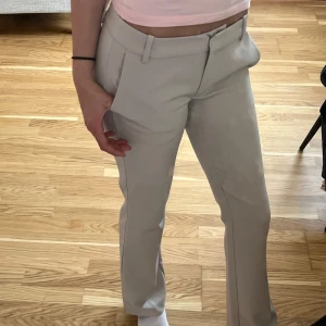 Beige kostymbyxor från BikBok - Snygga beige kostymbyxor från BikBok i storlek 34. Byxorna har en elegant och stilren design med låg midja och bootcut. Perfekta för en chic look. De har hällor för bälte och diskreta fickor baktill. Dem är knappt använda. Ny pris 500kr💗