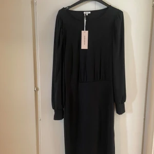 Svart klänning med ballongärmar från Bubbleroom - Elegant svart klänning från Bubbleroom med långa ballongärmar och en stilren design. Perfekt för en chic look. Klänningen har en klassisk passform och är tillverkad i ett mjukt material.