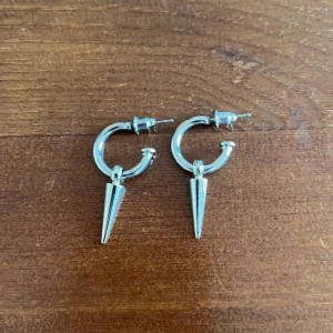 Silverfärgade örhängen med konformad detalj - Snygga silverfärgade örhängen med en cool konformad hängande detalj. Perfekta för att ge din outfit en edgy touch. Passar både till vardag och fest. Använd 1 gång