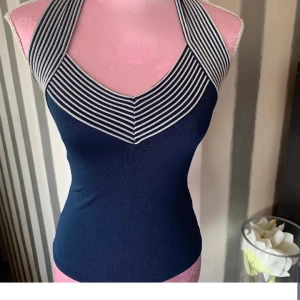 Mörkblå randig halterneck topp - Snygg mörkblå halterneck topp med vita ränder. Toppen har en åtsittande passform och är perfekt för en stilren look. Den ärmlösa designen ger en modern touch.