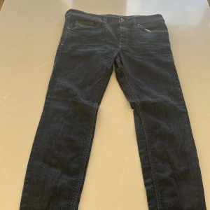 Mörkblå jeans från Diesel - Säljer ett par mörkblå jeans från Diesel med en slim passform. Jeansen har klassisk femficksdesign och knappgylf. Perfekta för en stilren look.