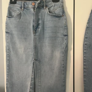 Ljusblå jeanskjol - Snygg ljusblå jeanskjol med klassisk femficksdesign och knappgylf. Kjolen har en rak passform och är perfekt för en avslappnad stil. Den är tillverkad i ett slitstarkt denimtyg och har en medellång längd.