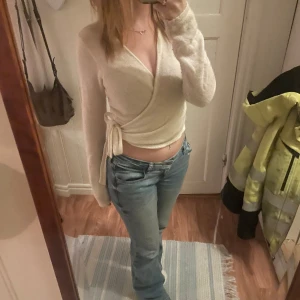 Vit omlottopp - Säljer en stilren vit omlottopp med långa ärmar. Toppen har en knytning i sidan. Säljs då den inte kommer till användning.