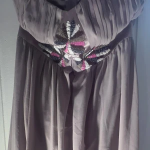 Grå/lila  axelbandslös festtopp från Lipsy London - Säljer en elegant grå axelbandslös topp från Lipsy London. Toppen har vackra pärldetaljer i svart, vitt och rosa på bysten och en dragkedja i ryggen. Perfekt för en speciell kväll! ✨