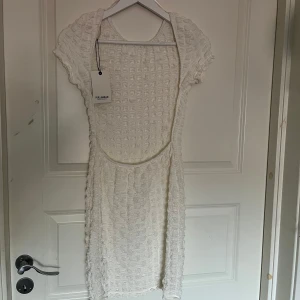 Vit klänning från Pull&Bear - Säljer en snygg vit klänning med öppen rygg från Pull&Bear med ett unikt strukturerat mönster. Klänningen har korta ärmar och en rund halsringning, perfekt för en stilren look. Passar perfekt till studenten men även till både vardag och speciella tillfällen. Pris går alltid att diskutera!💕