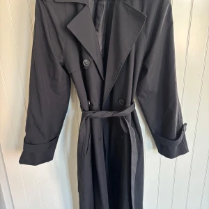 Svart trenchcoat/kappa med bälte - Superfin svart trenchcoat/ kappa med ett bälte i midjan. Den är använd fåtal gånger och har inga tecken på användning, skulle säga nyskick💖 