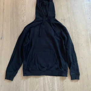 Svart hoodie med ficka framtill - Säljer en klassisk svart hoodie med en stor ficka framtill och justerbar huva. Perfekt för en avslappnad stil. Passar till det mesta och är superbekväm.