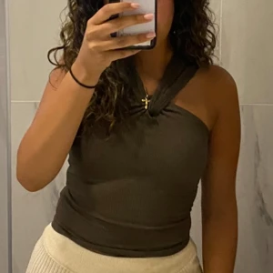 Brun ribbad halterneck topp - Snygg brun halterneck topp med twistad knut framtill. Ribbad struktur som ger en cool vibe och sitter tight mot kroppen. Perfekt för dig som gillar att sticka ut med detaljer och vill ha en trendig look. Passar till både jeans och kjol.