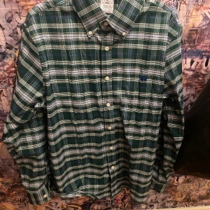 Rutig/rutig skjorta - Säljer en riktigt snygg skjorta ifrån Brooks Brothers. Den är randig/rutig i en snygg grön färg. Den är i bra skick och väldigt skön att bära. Storlek M, modellen på bilden är 181, 68 kg. Hör av dig vid intresse eller funderingar 😀 🌸.