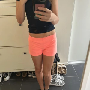 Neonrosa shorts från No Boundaries - Säljer ett par neonrosa shorts från No Boundaries i storlek XS. De har elastisk midja, kort passform och små slitsar på sidorna. Materialet är mjukt och består av 60% bomull och 40% polyester, vilket gör dem riktigt sköna och lätta för varma dagar.