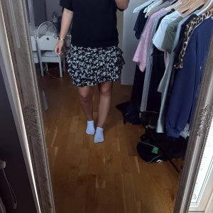 Svart blommig volangkjol  - Supersöt svart kortkjol från SHEIN med vitt blommönster och flera volanger. Kjolen har en flowy passform och är perfekt för dig som gillar en lekfull och trendig stil.