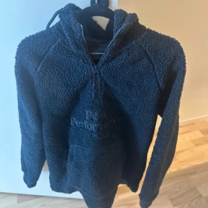 Mörkblå fleece hoodie Peak Performance - Säljer en mörkblå hoodie från Peak Performance i mjuk och fluffig fleece. Tröjan har huva med snörning, half zip och stor magficka. Broderad logga framtill. Perfekt för kalla dagar när du vill vara både chill och varm.