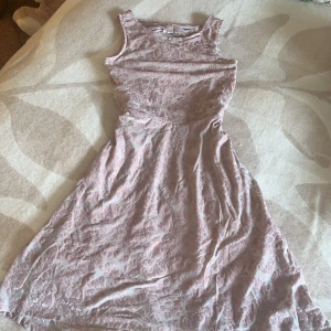 Ljusrosa klänning med rosett och mönster - Superfin ljusrosa klänning med blommigt mönster i sammet och en söt rosett i ryggen. Klänningen är ärmlös och har en rund halsringning. Materialet är mjukt och har en lyxig känsla med vacker struktur. Passar perfekt när du vill känna dig extra fin.