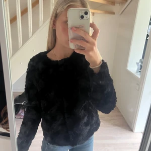 Svart fluffig päls-tröja - Mysig svart jacka med fluffig päls-look och rund hals. Långärmad och loose passform, perfekt för dig som gillar att sticka ut med en cool och mjuk vibe. Passar till jeans eller kjol och är superbekväm att ha på sig under kyliga dagar.