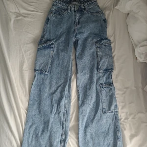 Blåa cargo jeans - Blåa cargo jeans från FB sister köpt på New Jorker. Använda ett fåtal ggr men efter som dem var för långa för mig så har det blivit ett litet hål bak längst ner och lite märken.