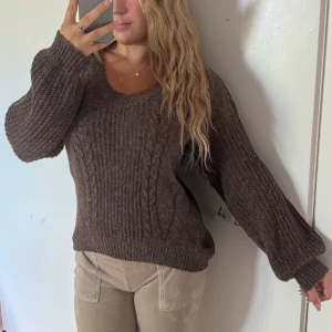 Brun stickad tröja med kabelmönster - Mysig brun stickad tröja med v-ringad hals och kabelstickat mönster framtill. Tröjan har långa ärmar och ribbade muddar vid ärmslut och nederkant. Perfekt för att hålla sig varm under kyliga dagar och passar till både jeans och mjukisbyxor. Aldrig använd har alltid bara varit i garderoben nästan gömd🤨  Storlek M men passar absolut en xs-m beroende på hur man vill den ska titta.  Jag är 166 och bör oftast S men kan variera xs-m