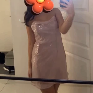 Ljusrosa glittrig axelbandslös klänning - Säljer en superfin ljusrosa kort klänning med glittriga paljetter. Klänningen är axelbandslös och har en snygg, figurnära passform som framhäver siluetten. Perfekt för dig som vill sticka ut med lite extra sparkle.