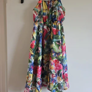 Färgglad blommig klänning Kate Morgan studio H&M stl 104 / 3-4 år - Superfin långklänning från Kate Morgan studio H&M med tropiskt blommigt mönster i starka färger som rosa, blå, grön och gul. Klänningen har smala axelband och ett flowigt fall, perfekt för sommarens varma dagar. Materialet är mjukt och lätt polyester.