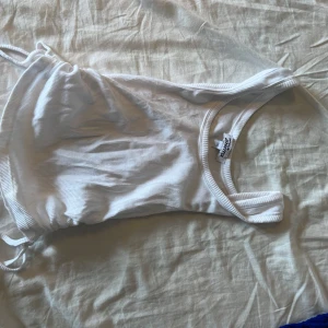 Vit linne - Supersnygg vit linne . Modellen har breda axelband och snörning i sidan för en cool och modern look. Perfekt för dig som vill ha en enkel men trendig stil på stranden i sommar.