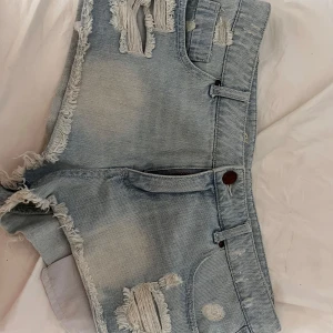 Ljusa jeansshorts från Denim Co. - Snygga ljusblå jeansshorts från Denim Co. med råa kanter och slitna detaljer framtill och baktill. Modellen är lågmidjad och har klassiska fickor samt knapp och dragkedja. Broderad text 'Cheeky short' på insidan av linningen. Använd några gånger men är för stora för mig som är 164cm så därför säljer jag💗