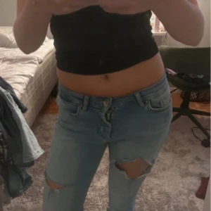 Ljusblå ripped jeans med hål - Säljer ett par ljusblå jeans med slitna hål över båda knäna. Jeansen har klassisk femficksmodell, small passform. Perfekta för en avslappnad och trendig look.