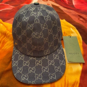 Blå keps - Snygg blå keps från med det klassiska GG-mönstret över hela kepsen. Justerbar rem baktill i blått skinn och insida i ljus bomull. Perfekt för dig som vill ha en lyxig och trendig accessoar med tydlig logga.