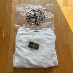 Vit Stone Island Tröja Storlek L | Pris kan diskuteras  - Vit sweatshirt från Stone Island med klassisk rund hals och ribbade muddar som jag fick som present. Tröjan har aldrig använts förut (gäller inte att prova på den). Tröjan är i Storlek L. Jag säljer tröjan pga att den e för stor på mig. All original förpackning finns och kommer skickas. Vid frågor kontakta gärna mig.
