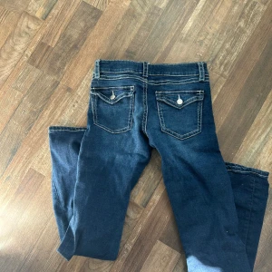 Mörkblå bootcut jeans med kontrastsömmar - Snygga mörkblå jeans med bootcut passform och tydliga vita kontrastsömmar. Byxorna har klassiska fem fickor, varav bakfickorna har lock och knappdetaljer. Tillverkade i stretchig jeanskvalitet för extra komfort. Är 170 cm lång men dessa byxor är 158cm
