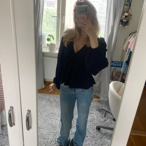 Mörkblå blus med v-ringning - Säljer en mörkblå blus med v-ringad hals och voluminösa långärmar. Blusen har en lätt struktur i tyget och sitter snyggt med en lite loose passform. Perfekt att styla med jeans eller kjol för en cool look.