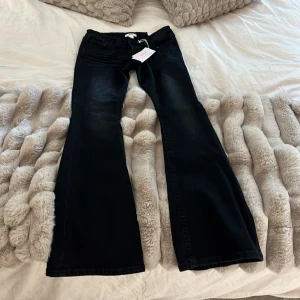 Svarta bootcut jeans från Gina Tricot - Snygga svarta jeans från Gina Tricot med bootcut passform och låg midja. Baktill har fickorna coola detaljer med silvriga nitar som ger extra edge. Jeansen är gjorda i klassiskt denim och har etikett och tags kvar. Perfekt för dig som gillar trendiga och statement byxor. Säljer dom för att dom var för långa och har aldrig använt. Prislappen sitter kvar. Paket storleken är mellan.