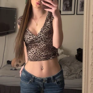 Leopardmönstrad croppad topp - Säljer en croppad topp med leopardmönster i beige och bruna toner. Toppen har v-ringad hals och korta ärmar, perfekt för dig som vill sticka ut. Materialet är mjukt och stretchigt, vilket gör den riktigt skön att bära. Passar dig som gillar trendiga och djärva plagg.