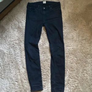 Svarta skinny jeans från Lee - Säljer ett par svarta skinny jeans från Lee med klassisk femficksdesign och smal passform. Jeansen har midwaist och är tillverkade i stretchigt denim som sitter snyggt och bekvämt. Perfekta för dig som gillar en stilren och enkel look.
