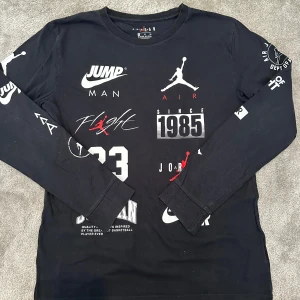 Jordan långärmad svart tröja - 🔥 Jordan Långärmad Tröja 🔥 Svart långärmad tröja från Jordan ⚫ med flera coola tryck och loggor i vitt och rött på framsidan och ärmarna 🔴🤍. 	•	👕 Crewneck och normal passform för klassisk stil 	•	🧵 Mjuk bomull som känns skön mot huden 	•	🌟 Perfekt för streetwear och en sportig look  En tröja som ger attityd och komfort i ett.