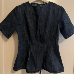 Mörk jeanstopp med kort ärm - Snygg mörkblå jeanstopp med korta ärmar och rund hals. Blusen har en figursydd passform. Perfekt att matcha med matchade byxor!