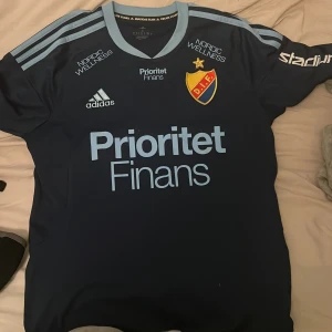 Djurgården fotbollströja Edvardsen #16 - Snygg Djurgården fotbollströja från Adidas med Edvardsen och nummer 16 på ryggen. Tröjan är mörkblå med ljusblå detaljer och tryck, klassiska Adidas-ränder på axlarna och DIF-emblem på bröstet. Materialet är lätt och andas, perfekt för match eller träning. Köpt från DIF butiken 