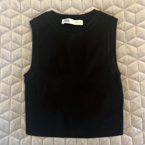 Svart croppad topp från Zara - En stilren svart croppad linnetopp från Zara som är ärmlös med rund halsringning🦋