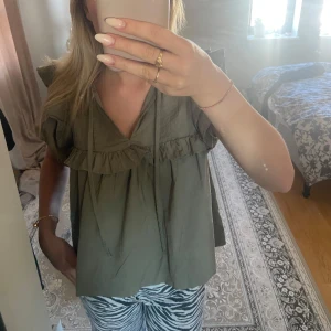 Olivgrön blus med volangdetaljer - Hej, jag säljer en söt topp ifrån Gina, perfekt färg till sommar och hösten🥰 använd ett par gånger i somras men inte längre! 
