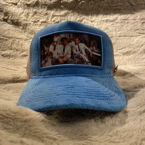 Blå Maggiore keps med foto-patch - Snygg blå keps från Maggiore med mesh i vitt och en unik patch framtill med foto-tryck. Framsidan är i mjuk frottéliknande material och baksidan har ett metallogo. Perfekt för dig som vill sticka ut med en cool accessoar helt ny !!!