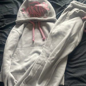 Grå Syna world tracksuit med rosa detaljer  - Säljer min gråa syna world ”central cee” tracksuit med rosa detaljer  och broderad text 'Forgive Me' i rosa vid benet. Baktill finns ett stort rosa ”Syna” -tryck. Byxorna har dragkedja vid benslut och är gjorda i mjukt bomullsmaterial. Perfekt för chill dagar och även vid street tillfällen! 