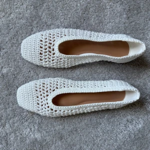 Vita virkade ballerinaskor från NA-KD - Säljer ett par vita ballerinaskor från NA-KD med snyggt virkad ovandel i polyester. Skorna har en rund tå och platt sula i skinn. Helt oanvända 