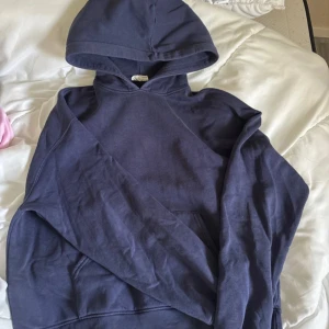 Mörkblå hoodie från Gina Tricot - Säljer en mörkblå hoodie från Gina Tricot, Basically Basics-kollektionen. Tröjan har huva, långa ärmar och en klassisk magficka framtill. Mjuk bomullskänsla och ribbade muddar vid ärmslut och nederkant. Perfekt för chill dagar eller när du vill vara extra comfy. (OBS hål vid armen men inget man tänker på elelr ser vid användning , den är oxå lite urtvättad därav priset)