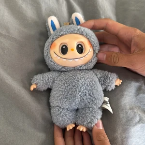 Labubu  - Ingen bok syns på bilderna, endast en söt och fluffig leksaksdocka med stort leende och kaninöron visas. Ingen information om titel, författare eller bokinnehåll kan identifieras.