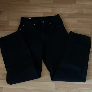 Svarta Levis 501 jeans wide fit - Säljer ett par svarta Levis 501 jeans med klassisk femficksdesign och raka, breda ben. Jeansen har knappgylf och detaljer i silver och koppar. Materialet är robust denim i bomull. Perfekt för dig som gillar en avslappnad och tidlös look.
