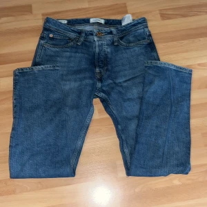 Blå jeans från Jack & Jones, 29/30 - Snygga blå jeans från Jack & Jones i klassisk straight fit. Modellen har fem fickor, gylf med dragkedja och knapp, samt coola detaljer på bakfickorna. Jeansen är tillverkade i slitstarkt bomullsmaterial och har en normal passform med midwaist.