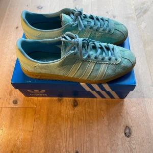 Adidas Gazelle ljusblå mocka sneakers - Säljer ett par Adidas Gazelle sneakers i ljusblå mocka med klassiska vita ränder på sidorna och gummisula. Skorna har snörning och rund tå. Knappt använda! Nypris 1300kr. Låda tillkommer. Skorv vid intresse!