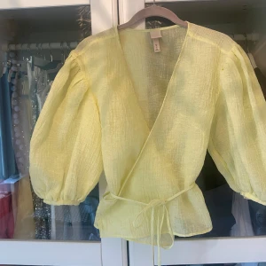 Gul wrap blus med korta ärmar  - Aldrig använd. Korta puffärmar. Snören att knyta runt midjan så den passar flera storlekar!