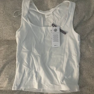 Vit linnetopp från Gina Tricot - Fräsch vit linnetopp från Gina Tricot, basically basics-kollektionen. Toppen har en rundad halsringning och är ärmlös med en clean, enkel design. Tillverkad i mjuk ekologisk bomull som känns skön mot huden. aldrig använd men lite skrynklig 🤍