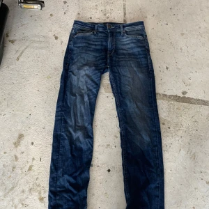 Mörkblå jeans - Säljer ett par jeans i mörkblå tvätt med snygga slitningar och klassiska fem fickor. Modellen är slim och har normal passform med rak midja. Jeansen är gjorda i mjukt denim och passar perfekt till en chill streetstil. Storleken är 28/32 och de är nästan helt nya